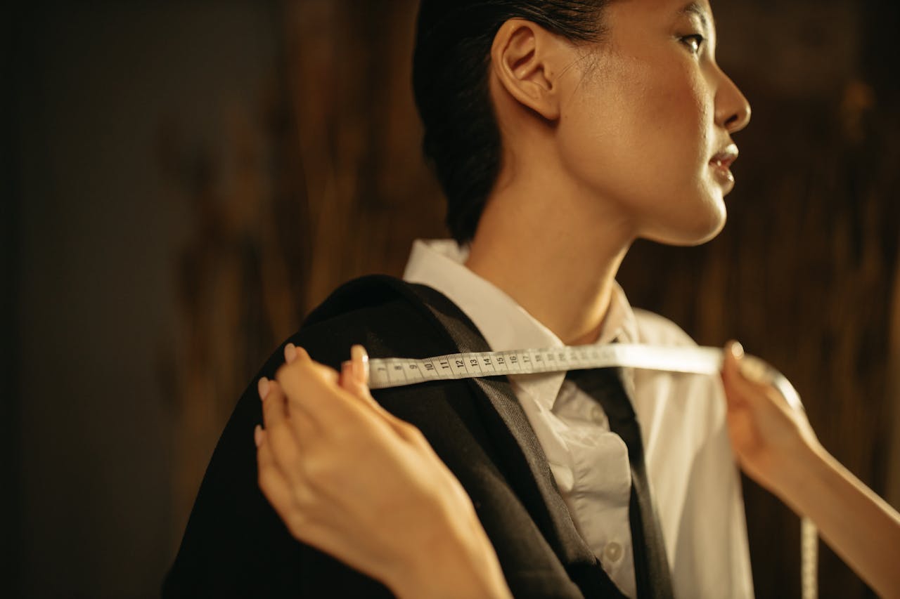 Close-up of an Asian woman in a vintage tailoring setup measuring a suit with precision.